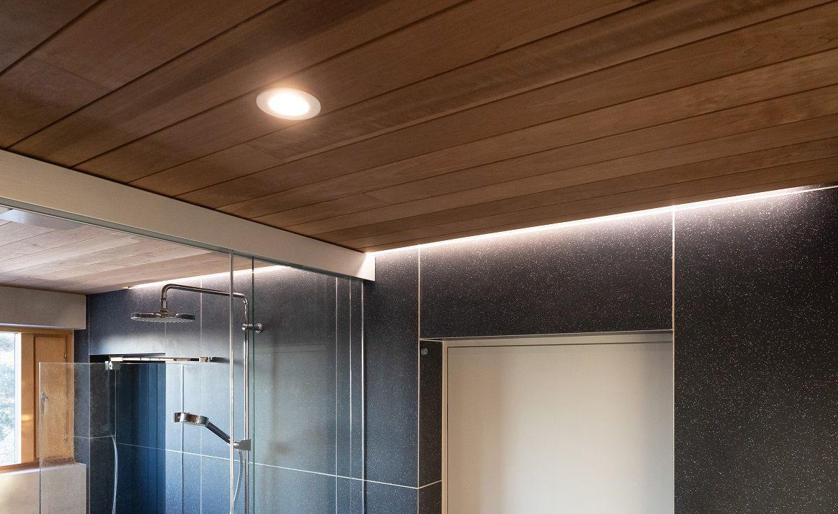 The sauna area is lit with spotlights recessed in the ceiling and indirect LED strip lighting along the wall next to the ceiling.